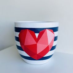 a cup with a red heart on it sitting on top of a white table next to a blue and white striped wall