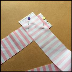 two pieces of pink and white striped paper with pins sticking out of the top one