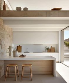 two stools sit in front of an island counter with white countertops and stone walls