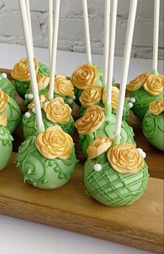 there are many green and yellow cake pops with flowers on them sitting on a wooden tray