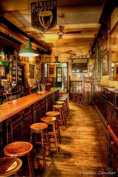 an old fashioned bar with wooden stools and green lights hanging from the ceiling above it