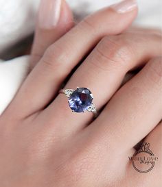 a woman's hand wearing a ring with an oval shaped tanzante and white diamonds