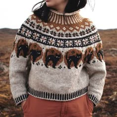 a woman standing in an open field wearing a sweater with elephants on it