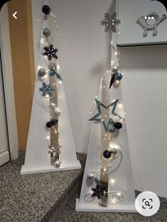 two white christmas trees decorated with lights and snowflakes are on the floor next to each other