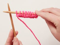 someone is knitting with pink yarn on a wooden stick