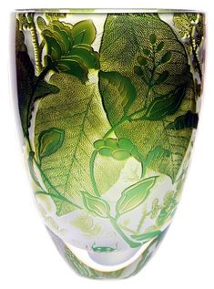 a green and white glass vase with leaves on the outside, in front of a white background