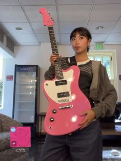 a woman holding a pink guitar in her hand and posing for the camera with it's neck up