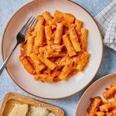 two plates filled with pasta and cheese on top of a blue table cloth next to a wooden cutting board