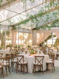 tables and chairs are set up in a tent for an outdoor wedding reception with greenery hanging from the ceiling