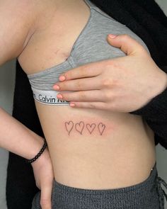 a woman's stomach with small hearts tattooed on the side by her arm and hand