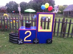 a train made out of cardboard sitting in the grass next to a fence with balloons