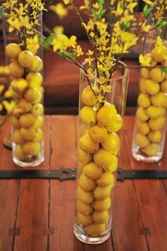 three vases filled with yellow flowers and lemons on top of a wooden table