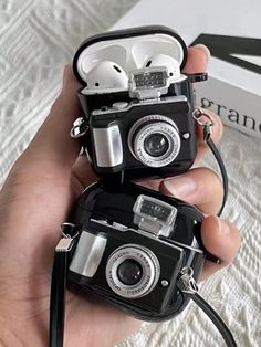 two small cameras sitting on top of a bed next to a box with ear buds