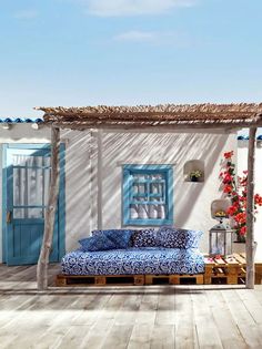 a bed sitting on top of a wooden floor next to a white building with blue doors