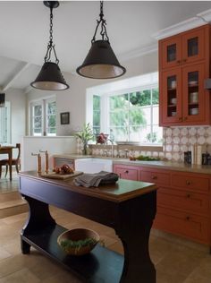 a kitchen with red cabinets and an island in front of the countertop, along with two hanging lights