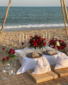 a table set up on the beach with flowers and candles for an outdoor dining area