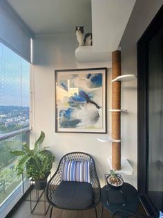 a cat sitting on top of a wooden shelf next to a chair in front of a window