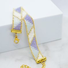 a gold chain bracelet with purple and white beads on top of a marble countertop