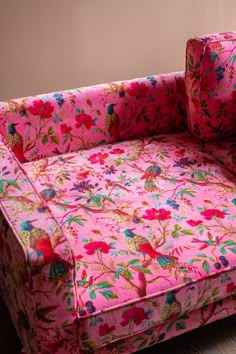 a pink floral couch sitting on top of a hard wood floor next to a wall