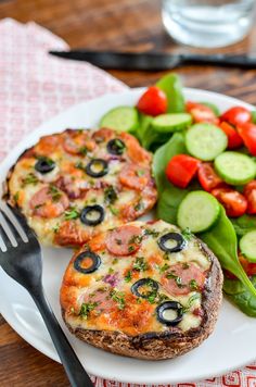 a white plate topped with two pizzas and veggies next to a fork