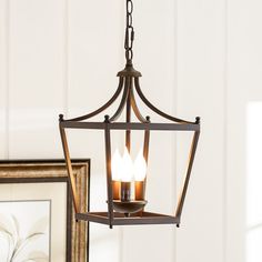 a hanging light fixture with two candles in it and a framed photo on the wall