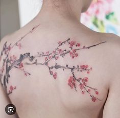 the back of a woman's shoulder with red flowers on it and branches in bloom