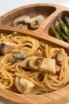 a wooden bowl filled with pasta and mushrooms on top of a white table next to asparagus