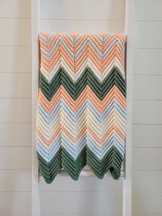 an orange and green crocheted blanket hanging on a white ladder next to a wall