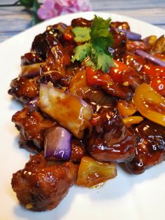 a white plate topped with meat covered in sauce and vegetables next to a purple flower