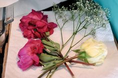 three different colored flowers on a white cloth next to silverware and utensils