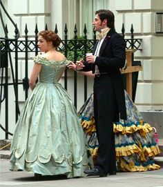 a man and woman dressed in period clothing standing next to each other on the street