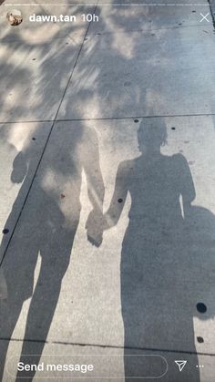 two people holding hands walking down the street with shadows on the sidewalk and one person's shadow