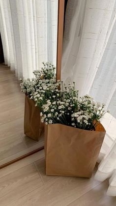 a brown paper bag filled with flowers sitting on top of a wooden floor next to a mirror