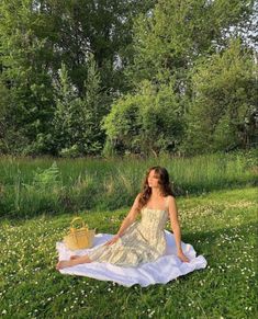 a woman is sitting on a blanket in the grass with a basket next to her