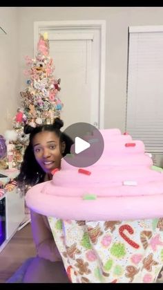 a woman holding up a giant cupcake in front of a christmas tree