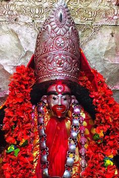 an elaborately decorated statue in front of a wall with red flowers and decorations on it