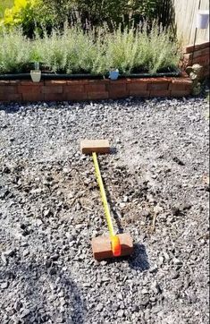 an orange and yellow plastic mallet sitting on top of gravel next to a garden