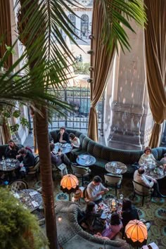 people are sitting at tables in the middle of a room with large windows and palm trees