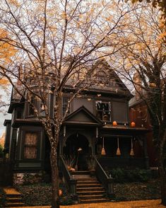 an old victorian style house with pumpkins on the porch and trees in fall colors