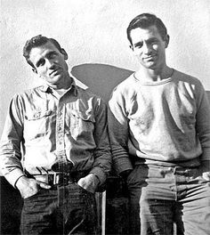 two men standing next to each other in front of a white wall with red writing on it