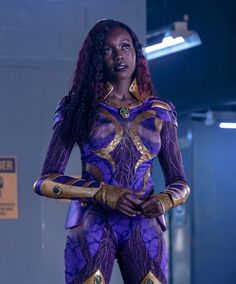 a woman dressed in purple and gold stands with her hands on her hips as she looks off to the side