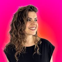 a woman with curly hair smiling and wearing a black shirt, against a pink background