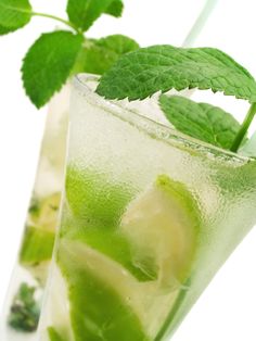 a glass filled with ice and limeade on top of a white table next to a green leaf