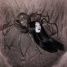 a woman with long black hair laying on top of a spider