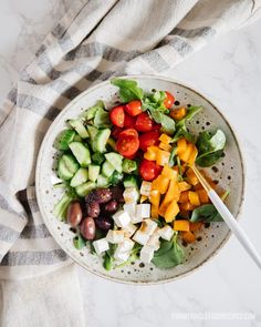 a white bowl filled with cucumbers, tomatoes and other vegetables on top of a marble counter