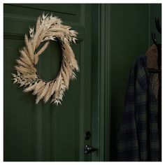 a green door with a wreath hanging on it's side next to a coat rack