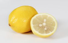 two lemons sitting next to each other on a white surface with one cut in half