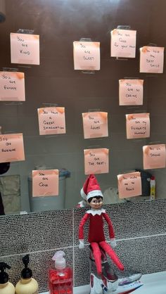 an elf is sitting on top of a sink in front of a mirror with notes attached to it