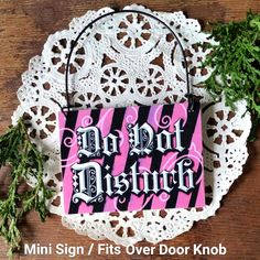 a pink and black sign sitting on top of a doily next to some plants