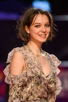 a young woman is smiling and wearing a floral dress with ruffles on it